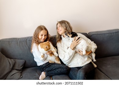 Mom and daughter are sitting on the couch at home and hugging their pets, a cat and a dog. Concept petrenthood - fur babies