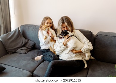 Mom And Daughter Are Sitting On The Couch At Home And Hugging Their Pets, A Cat And A Dog. Concept Petrenthood - Fur Babies