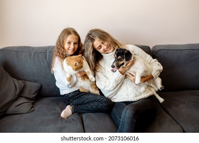 Mom and daughter are sitting on the couch at home and hugging their pets, a cat and a dog. Concept petrenthood - fur babies