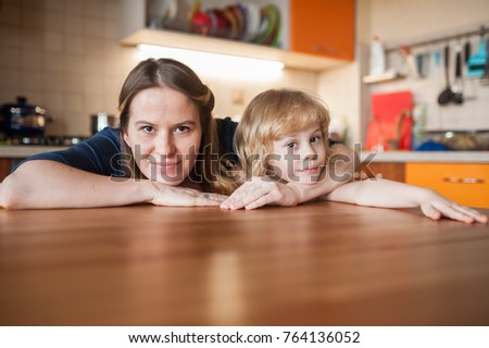 Mom and daughter are sitting at a round table in the orange kitchen, hugging and looking at the camera