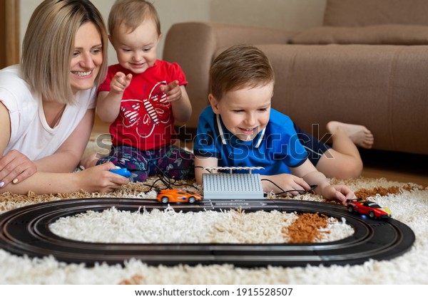 Mom and\
daughter and son play racing on the\
carpet.