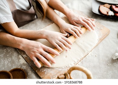 mom and daughter spend leisure time in the kitchen together. Top view of female and children's hands rolling out dough with a rolling pin on a wooden board in flour - Powered by Shutterstock