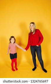 Mom And Daughter Standing On The Yellow Background In Studio