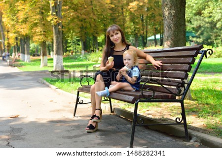 Mom and daughter in the summer eat ice cream on the bench