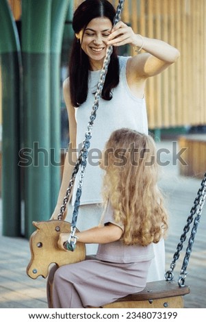 Mom and daughter swing on a swing. Caucasian woman and little girl have fun on the playground. Lifestyle and people concept.