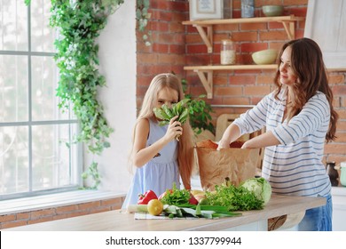 Mom And Daughter Take Out Vegetables And Fruits From A Paper Bag / Mom And Daughter Unpack Purchases In The Kitchen / Copy Space