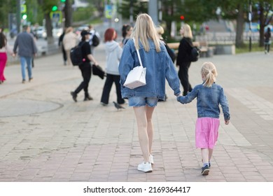 Mom and daughter are walking down the street of the city.Walk around the city in the evening.