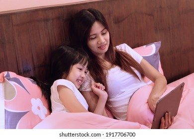 Mom And Daughter Watch Movie Together On Bed At Night. Family Activity At Home Before Bed Time. 