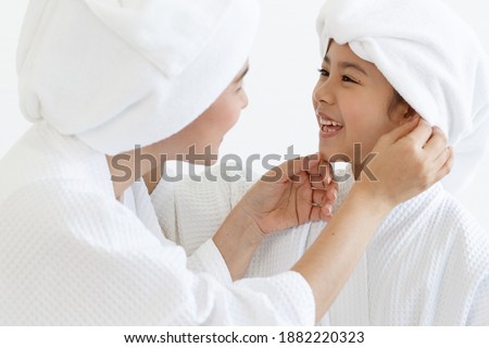 Mom and daughter wearing spa dress talking and teasing with happiness in spa with white cloth and towel-covered around head. Idea for health care and relaxing and family relationship.