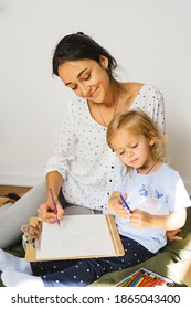 
Mom And Daughter Are Writing A Letter To Santa Claus On The Background Of A Christmas Tree And Gifts. Young Woman Teaches Little Cute Girl To Draw A New Year Card. Family Cozy Moments.
