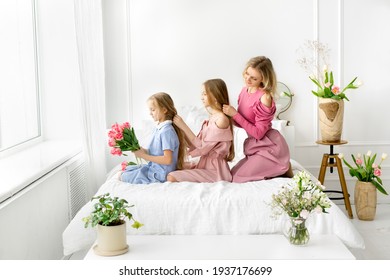 Mom and daughters comb and braid each other's hair. Daily morning care. A bouquet of tulips in the hands of a girl. Care for long hair. Smooth and silky hair after shampooing. - Powered by Shutterstock