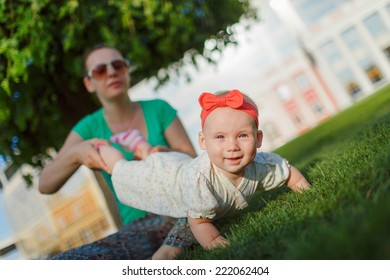 Mom Doing Yoga With Your Child. Baby Crawling On The Grass On A Background Of Sitting His Mom. The Kid Runs Away From His Mother.