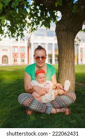 Mom Doing Yoga With Your Child. Baby Crawling On The Grass On A Background Of Sitting His Mom. The Kid Runs Away From His Mother.