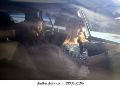 Mom Driving Car While Her Daughter Sitting On Back Seat And Using Digital Tablet