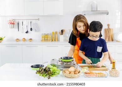 Mom Enjoy Family Education For Son At Kitchen By Standing Behind And Catch His Hands To Teach Cutting Vegetable Into Pieces And Kid Pay Attention To Learn From Her At Home