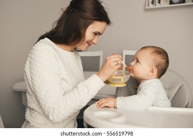 Mom feeding her baby girl with a spoon. Mother giving food to her eight-month child at home. Baby food.