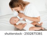 mom feeds the baby with a bottle of milk or formula, feeding the baby in her arms, a young mother feeds the newborn baby at home on the bed.