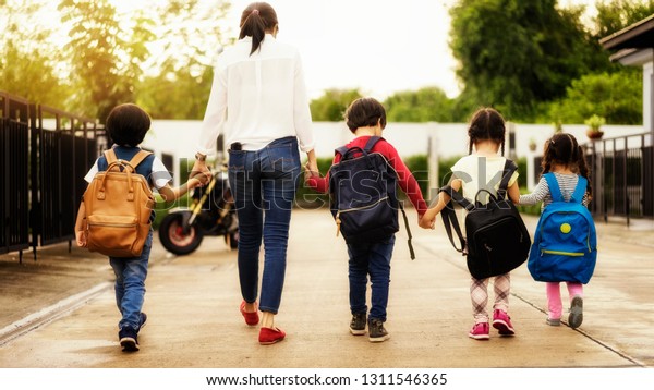 Mom\
and four kindergarten kids holding hand carry schoolbag walking to\
school bus.preschool concept.first day of\
semester