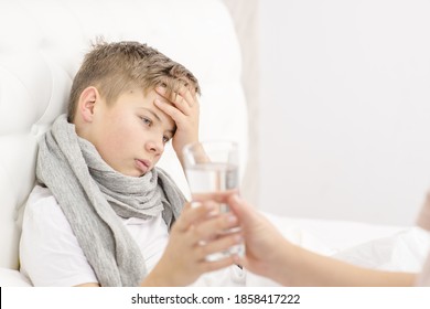 Mom Gives A Sick Little Boy A Glass Of Water While Him Lying On The Bed At Home. An Unhealthy Child Drinks Water From Glass. Cold Season.