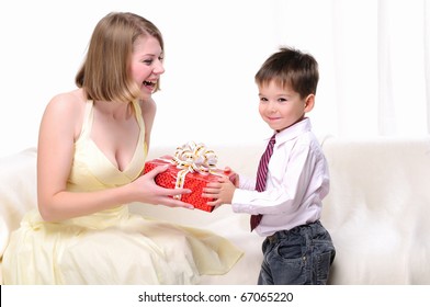 Mom Giving A Gift To His Son Sitting On A White Sofa.