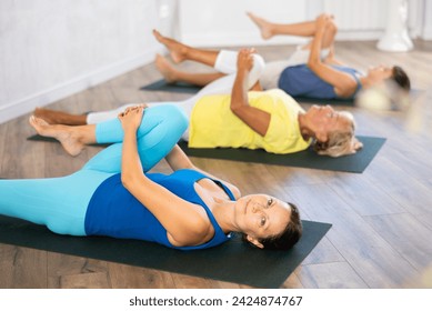 Mom, grandmother and teen grandson performing preparatory stretching, lying on back, bent one leg at knee and raised it to chest. Family three generations actively spend time in gym. - Powered by Shutterstock