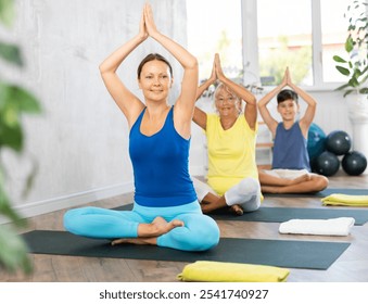 Mom, grandmother and teen grandson performing sitting half lotus position of Ardha Padmasana Sidhasana with greet namaste. Family three generations actively spend time in gym. - Powered by Shutterstock