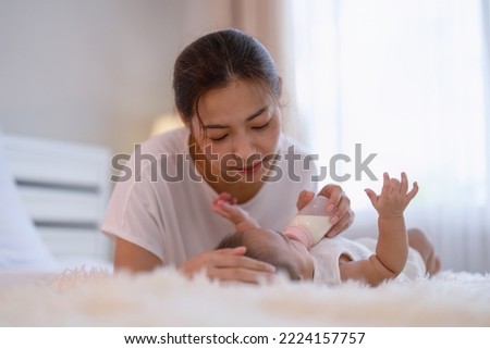 Mom happy teasing feed milk to asian infant baby new born on bed look at mother face