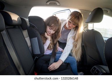 Mom Helping Her Daughter To Fasten Belt In Child Car Seat