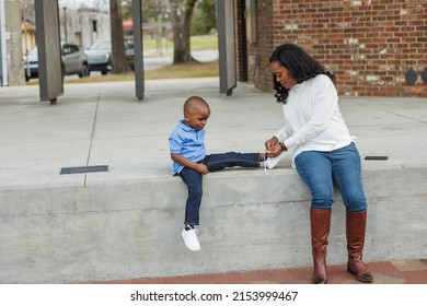 A mom helping her son by tying his shoes while outside. - Powered by Shutterstock