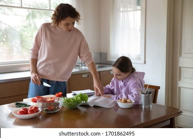 Mom helping teenage daughter with studies while cooking at kitchen table. Young adult parent mother and teen child girl doing everyday activities enjoying family casual lifestyle at home together. - Powered by Shutterstock