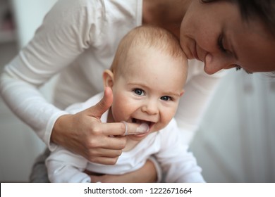 Mom helps to brush the teeth of a happy baby, Hygiene of the baby’s mouth, brushes her teeth with a special nozzle.