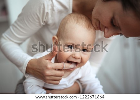 Mom helps to brush the teeth of a happy baby, Hygiene of the baby’s mouth, brushes her teeth with a special nozzle.