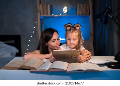 Mom Helps Child Daughter Do Homework At Home Using Digital Tablet. Child Studying Late At Night. Children, Family, Education Concept