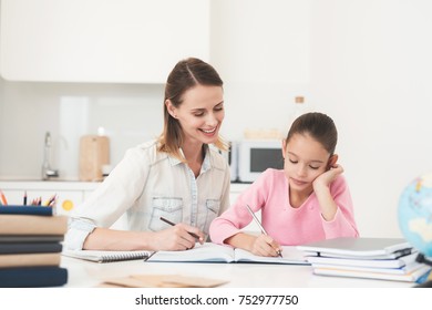 Mom helps my daughter do her homework in the kitchen. Mom and daughter are trying to solve the task. They are in a good mood and smile.