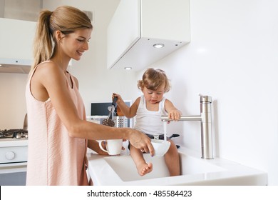 Mom With Her 1,4 Years Old Child Washing Dishes In The White Kitchen Interior