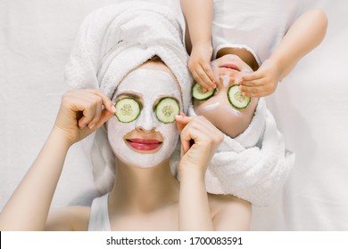 Mom and her 2 years old baby girl having fun together, making clay facial mask and cucumber slices on eyes. Mother with child doing beauty treatment together. Family time, spa and beauty, mothers day