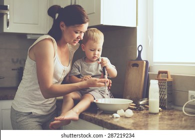 Mom With Her 2 Years Old Child Cooking Holiday Pie In The Kitchen To Mothers Day, Casual Lifestyle Photo Series In Real Life Interior