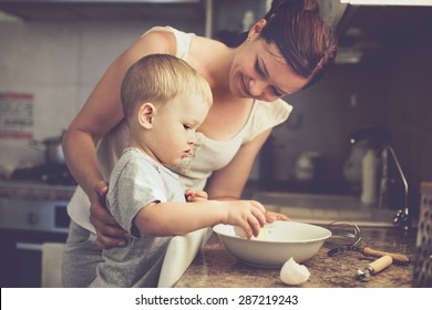 Mom With Her 2 Years Old Child Cooking Holiday Pie In The Kitchen To Mothers Day, Casual Lifestyle Photo Series In Real Life Interior