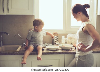 Mom With Her 2 Years Old Child Cooking Holiday Pie In The Kitchen To Mothers Day, Casual Lifestyle Photo Series In Real Life Interior