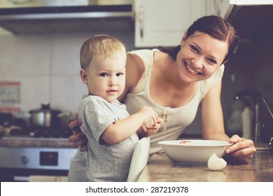 Mom With Her 2 Years Old Child Cooking Holiday Pie In The Kitchen To Mothers Day, Casual Lifestyle Photo Series In Real Life Interior