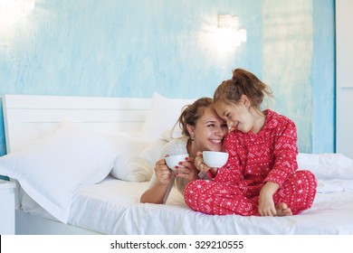 Mom With Her 6 Years Old Little Daughter Dressed In Winter Pajamas Are Relaxing And Playing In The Bed At The Weekend Together, Lazy Morning, Warm And Cozy Scene.