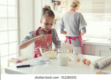 Mom With Her 9 Years Old Daughter Are Cooking In The Kitchen To Mothers Day, Lifestyle Photo Series In Bright Home Interior