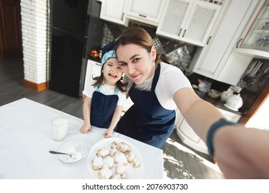 Mom and her daughter bake cookies at home in the modern kitchen and making selfie - Powered by Shutterstock