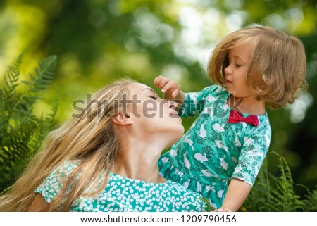 Mom with her daughter in the park. Happy and active little girl in a green dress playing with her young and beautiful mom during a walk on a summer day. Happy childhood. Positive emotions and energy