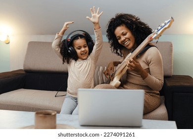 Mom with her daughter playing electric guitar together at home, happy family - Powered by Shutterstock