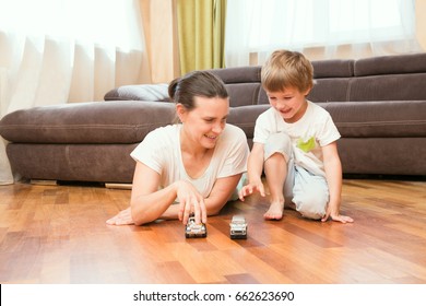 Mom And Her Little Son Play Car Toys In Their Living Room. The Happy Family Spends Time Together At Home.