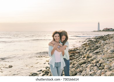 Mom And Her Teenage Daughter Hugging And Smiling Together Over Sunset Sea View.Beautiful Woman Relaxing With Her Child.