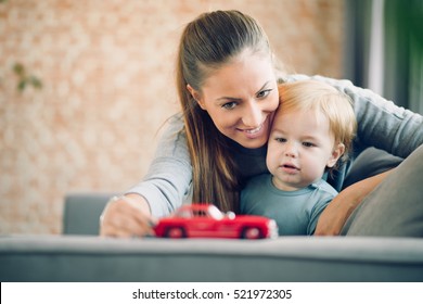 Mom And Her Toddler Son Plays With Red Car In Their Cosy Living Room