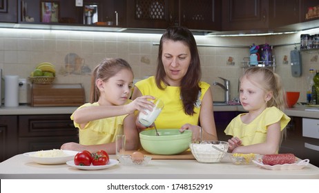 Mom and her two daughters have fun in the kitchen. Mom teaches kids how to make pizza. Happy mother and happy children are cooking dinner together in the kitchen.