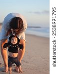 Mom with his daughter at the beach teaching her newborn how to walk.